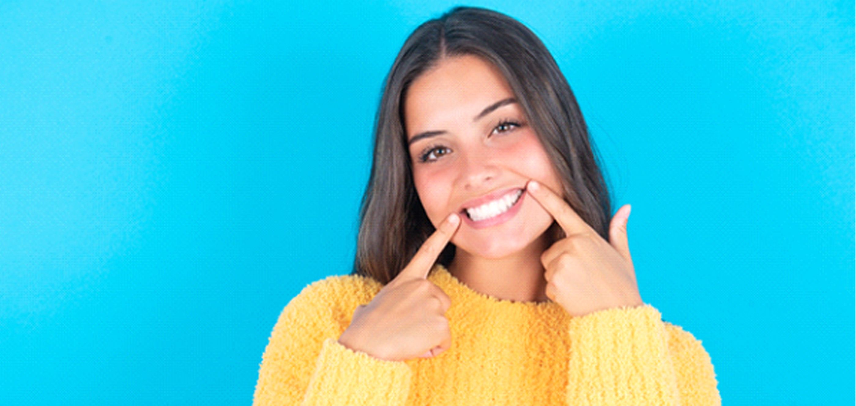 Woman in yellow sweater pointing at her beautiful smile
