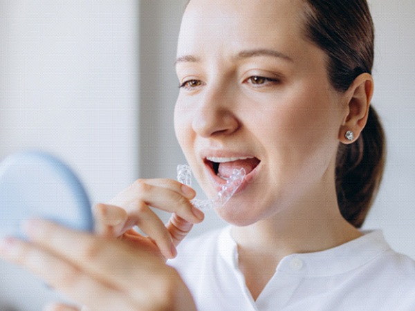 Person placing orthodontic retainer on her teeth